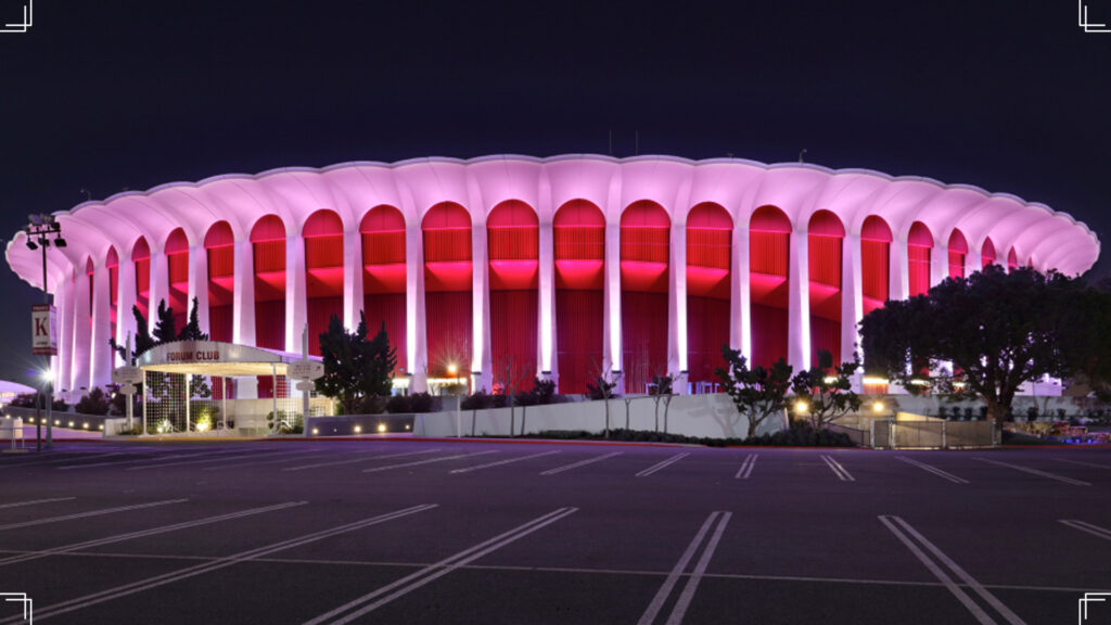 The Kia Forum in Inglewood, CA is lit up with a purplish and red color.