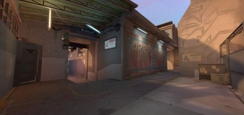 An alleyway filled with graffiti ends at a set of stairs that lead into a more open area of Sunset, the new VALORANT map.