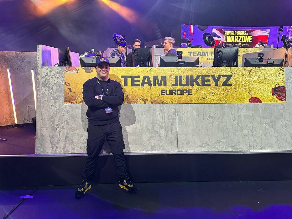 Jukeyz stands with his arms folded in front of his team's banner at the World Series of Warzone.
