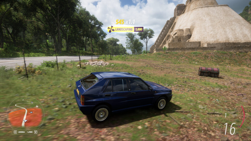 A car approaches the treasure chest in the grass near a temple.