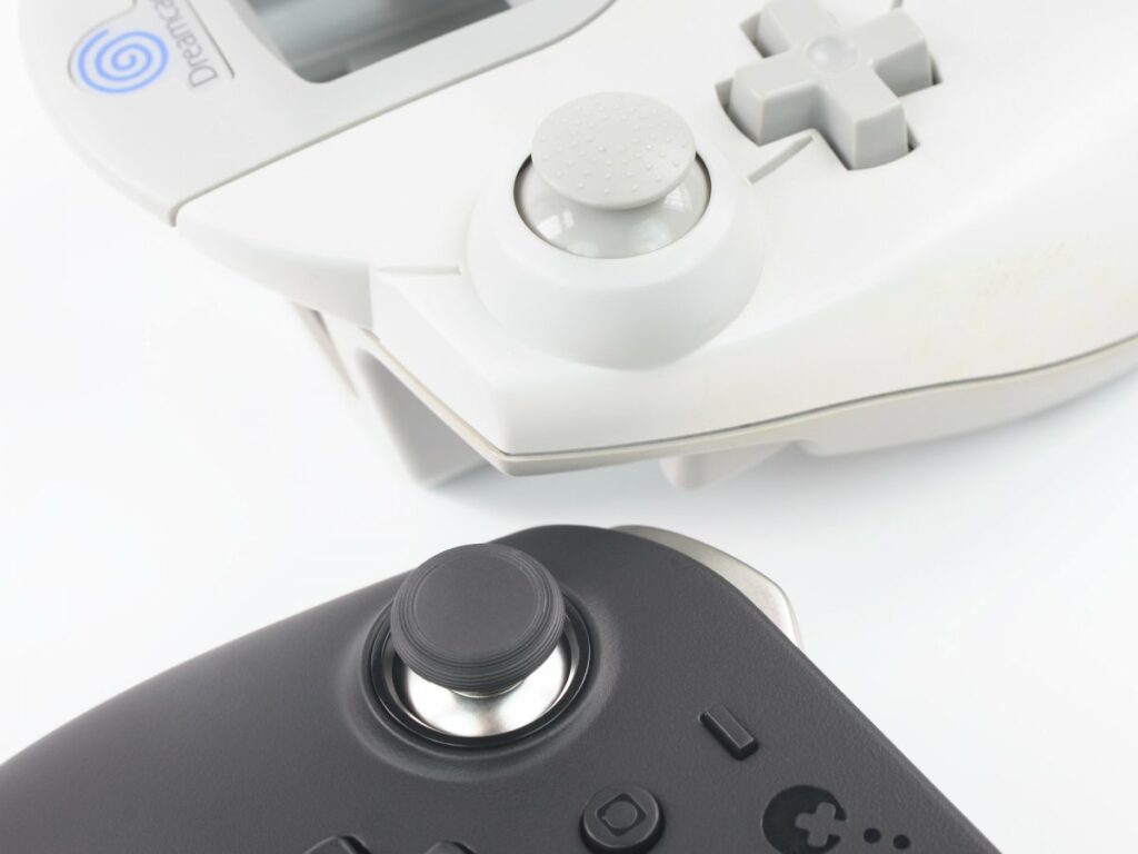 Shows two examples of controllers with Hall effect joysticks, the Sega Dreamcast controller and the GuliKit King Kong 2 Pro, right next to each other.