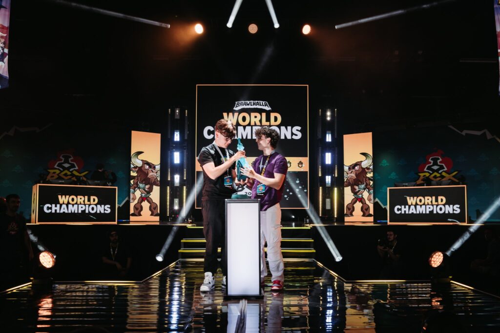 It's a photo of Brawlhalla 2v2 World Champions 2024 at BCX 2024: lores and Kyna are taking their trophy on the stage