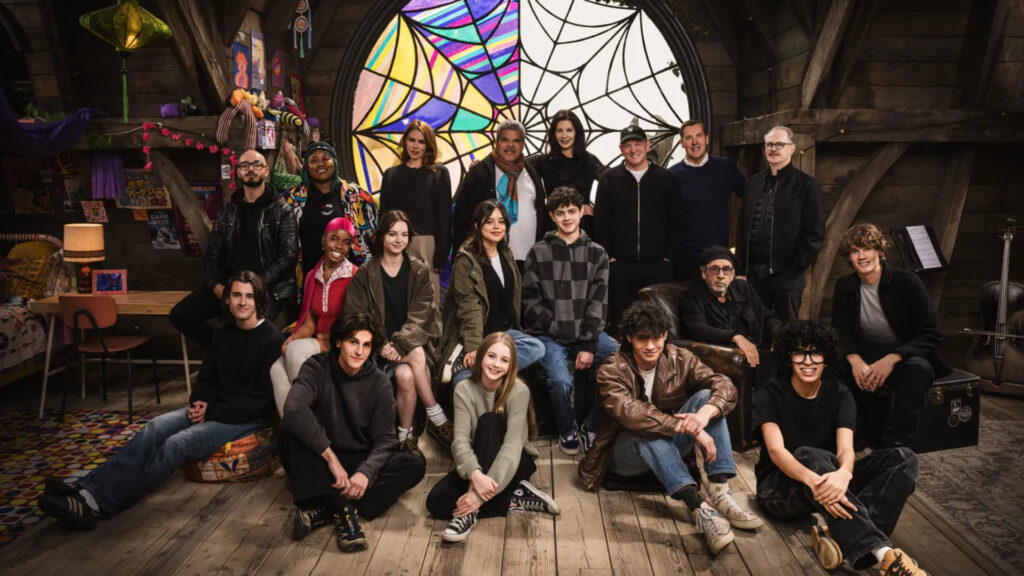 From left to right, Georgie Farmer, Victor Dorobantu, Luyanda Unati Lewis-Nayo, Joy Sunday, Owen Painter, Emma Myers, Billie Piper, Jenna Ortega, Evie Templeton, Luis Guzmán, Isaac Ordonez, Catherine Zeta-Jones, Alfred Gough, Noah Taylor, Miles Millar, Tim Burton, Steve Buscemi, Moosa Mostafa, and Hunter Doohan on the set of Wednesday Season 2.