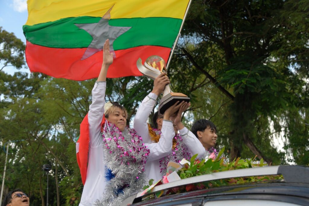 Yangon Galacticos hold their trophy with Myanmar flag behind them