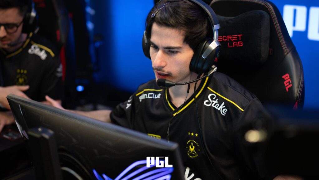 It’s a photo of Counter-Strike 2 player Shahar "flameZ" Shushan from Team Vitality during the Swiss Stage of the CS2 esports tournament PGL Cluj-Napoca 2026 — in front of a monitor, greets a teammate with a fist bump during a match.