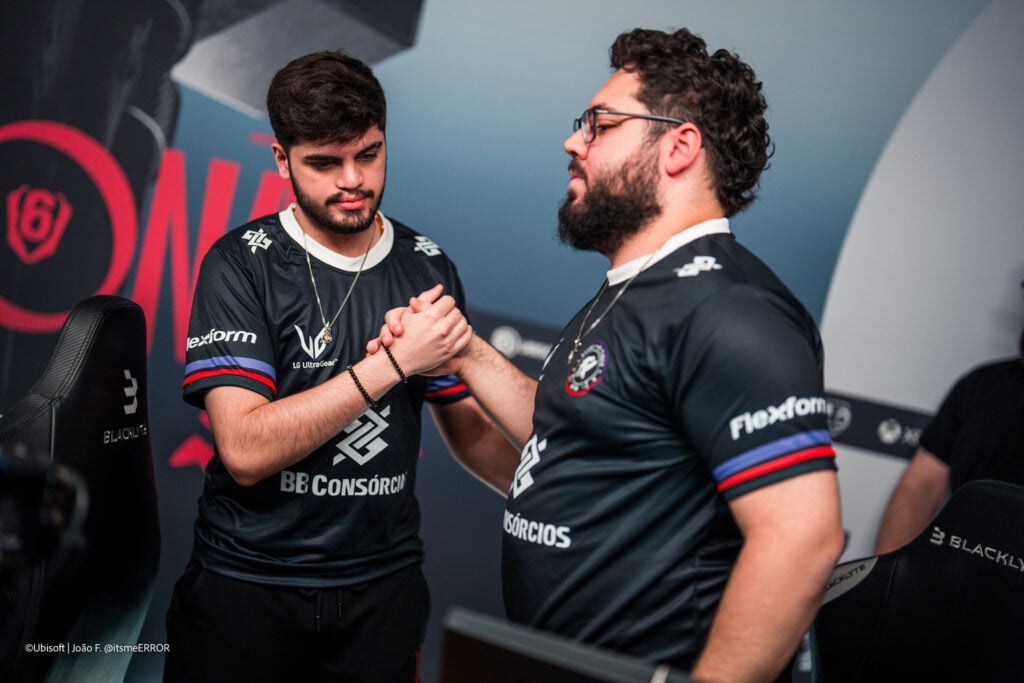 It’s a photo of two Rainbow Six Siege X esports players from team Fluxo W7M during the Playoffs stage of the tournament Six Invitational 2026: they congratulate each other after winning a game, a man handshake.