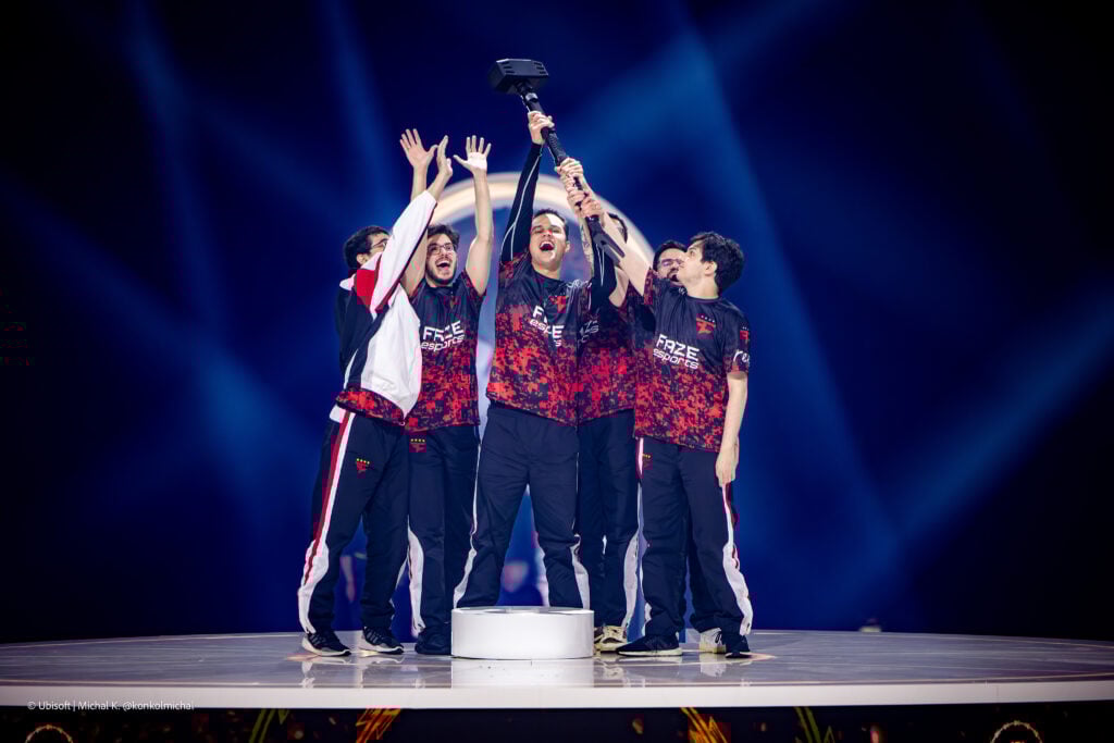 The photo features the R6 esports players from the team FaZe Clan on a stage holding the trophy of the tournament Six Invitational 2026 — an iconic Hammer.